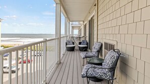 A covered balcony with wicker furniture, a view of the beach, and a parking area in the background.