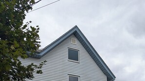 A two-story house with a blue door, a small front porch, and two well-maintained evergreen shrubs. - Modern NewlyFurnished Acadia Apt (Ellsworth)