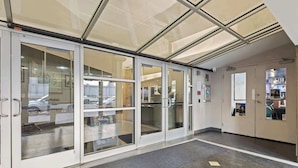 A modern hotel entrance with glass doors, a reception area, and a view of the street outside.