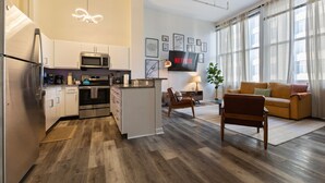 A modern kitchen with stainless steel appliances, a dining area with a table and chairs, and a living room with a sofa and a TV.