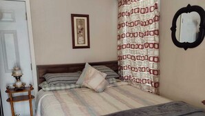 Quarto com cama, mesa de cabeceira, abajur, quadro na parede e cortina estampada.