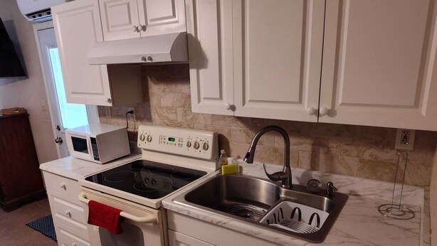 Uma cozinha com armários brancos, fogão, forno, micro-ondas, pia e bancada de mármore.