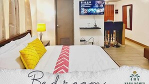A bedroom with a bed, a TV mounted on the wall, a desk, and a chair. - Airport Condo across NAIA T3 (Pasay)