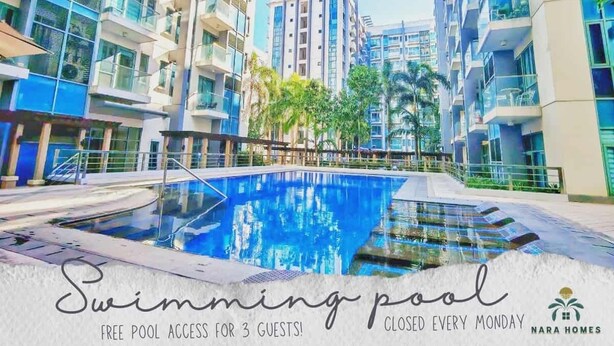 A swimming pool surrounded by modern buildings with balconies, and a sign indicating free pool access for 3 guests. - Airport Condo across NAIA T3 (Pasay)
