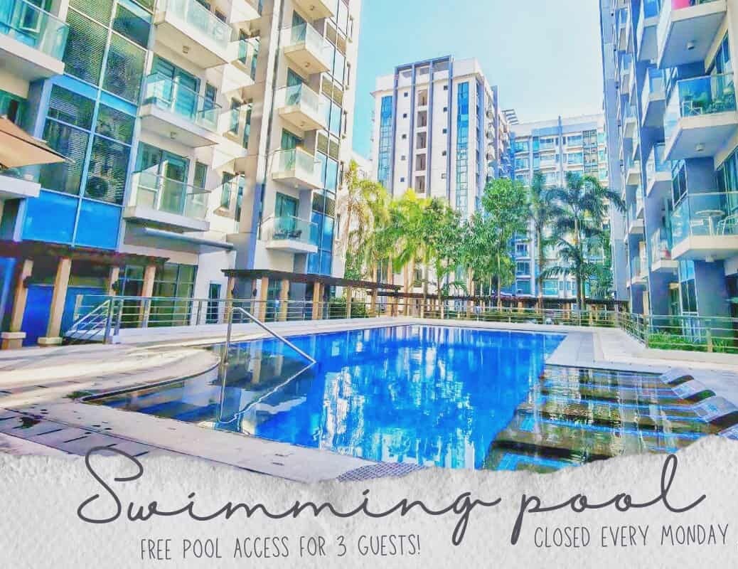 Piscina rodeada de edificios modernos con balcones, y un cartel que indica acceso gratuito a la piscina para 3 personas.