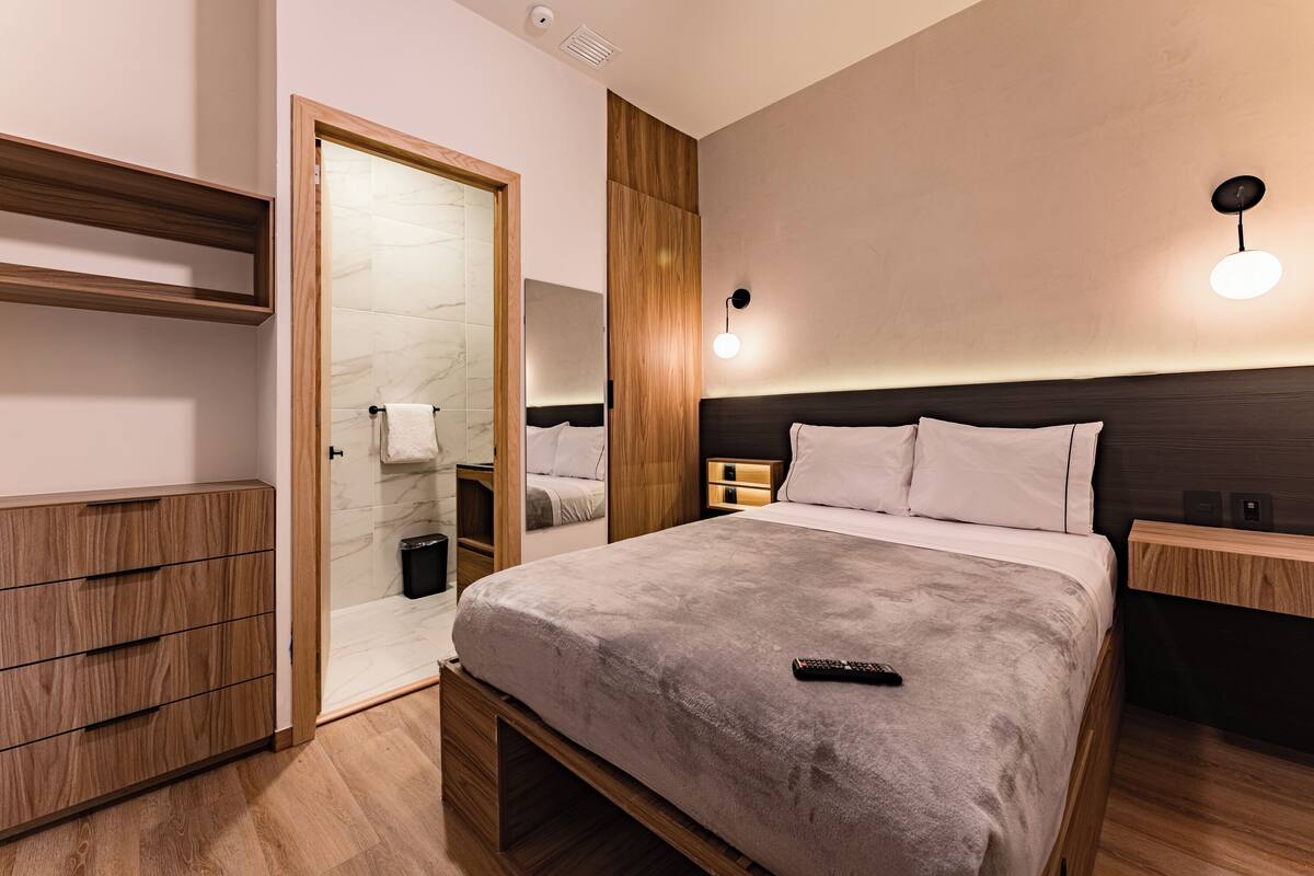 Une chambre d’hôtel moderne dotée d’un grand lit, de meubles en bois, d’une armoire intégrée et d’une salle de bain avec une douche à parois de verre.