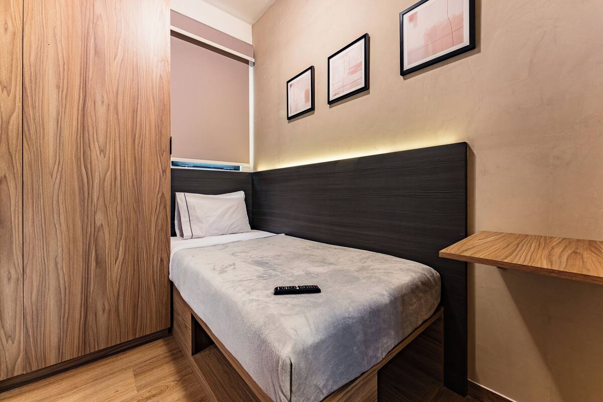 Un lit simple avec une tête de lit sombre, une table de chevet et une étagère fixée au mur.