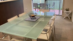 Une table à manger avec un plateau en verre, des chaises, une petite lampe de table et une plante en pot posée sur un support blanc.