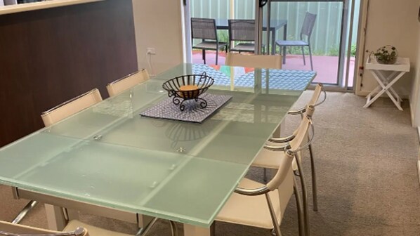 A glass-top dining table with chairs, a small table lamp, and a potted plant on a white stand.