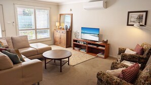 Un salon comprenant un canapé, une table basse ronde, un téléviseur posé sur un meuble en bois et un fauteuil à motifs floraux.