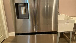 Ett kylskåp i rostfritt stål med en is- och vattendispenser, placerat i ett kök med en vit bänkskiva och ett trägolv.