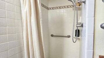 A small, tiled shower room with a showerhead, a handrail, and a curtain.