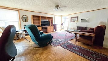 A living room with a teal armchair, a wooden coffee table, a TV stand, and a patterned rug.