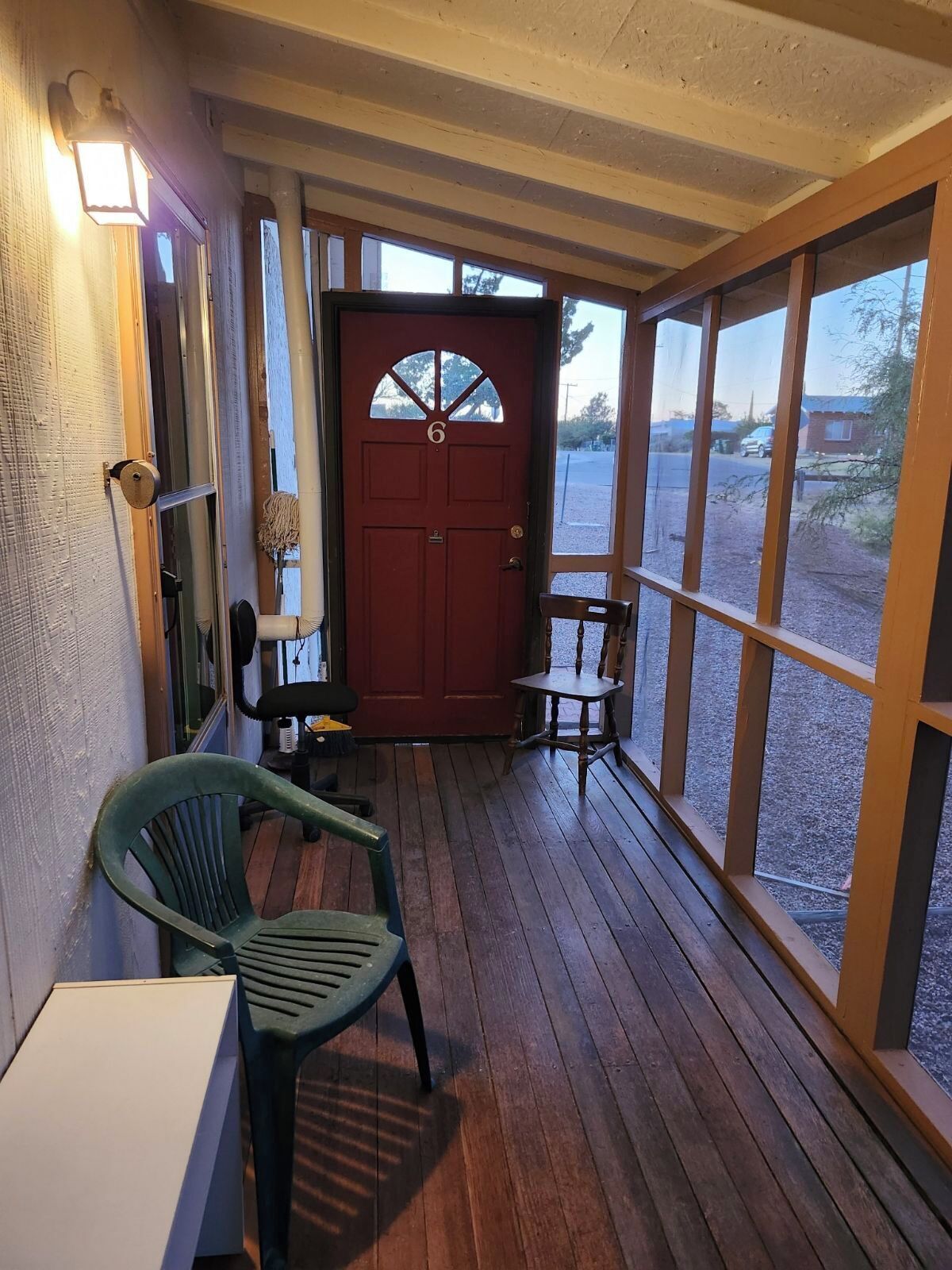 A wooden porch with a red door, a green chair, and a table.