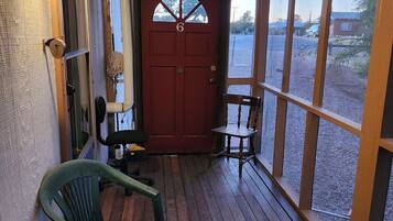 A wooden porch with a red door, a green chair, and a table.