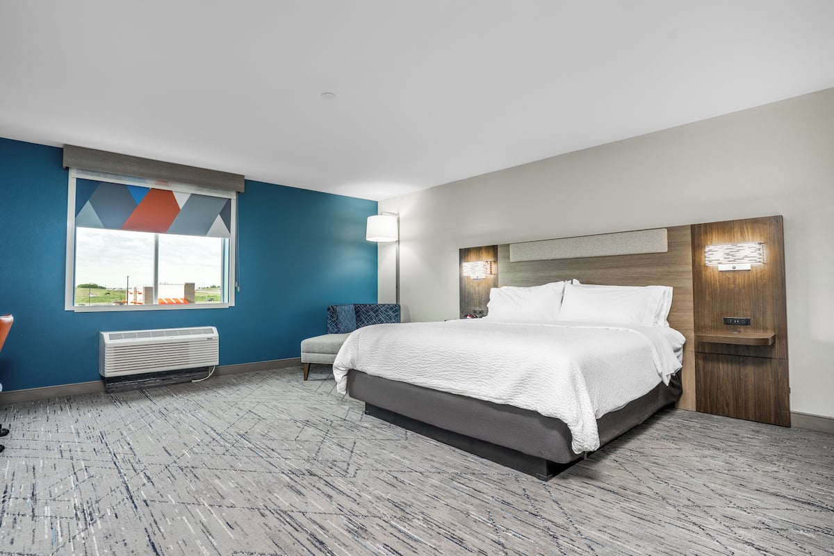 A modern hotel room with a large bed, a desk, a chair, and a window with a view.