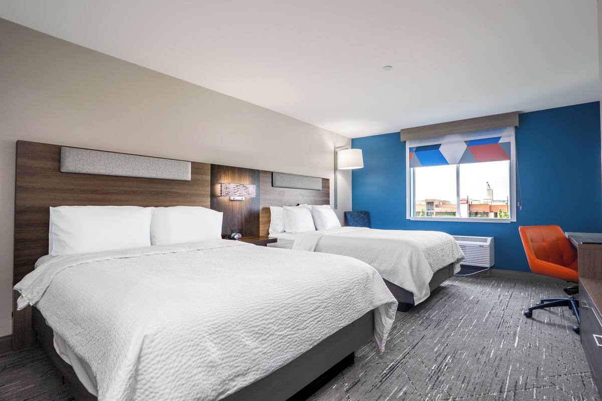 A hotel room with two beds, a desk, and a chair.