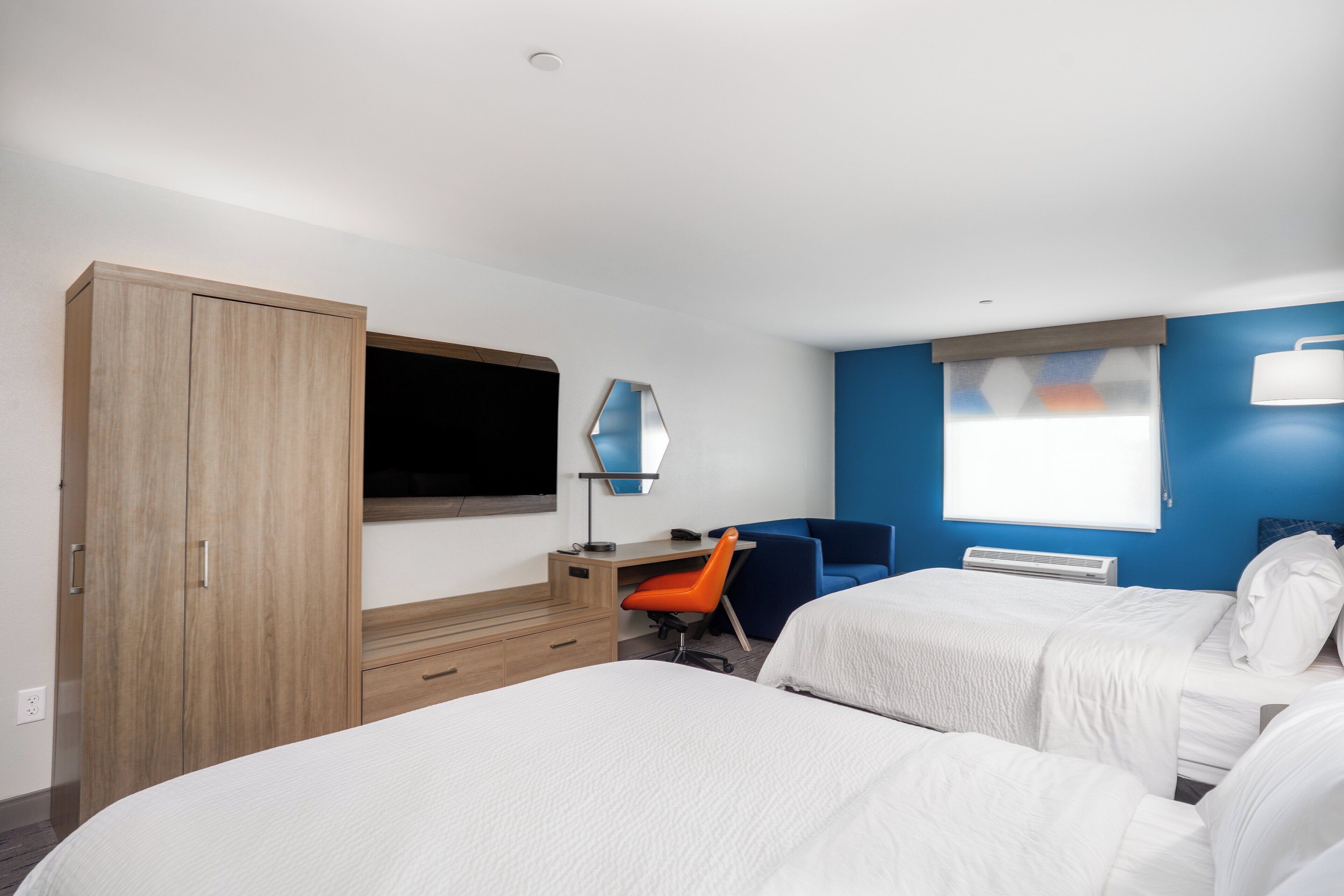 A hotel room with two beds, a desk with a chair, a TV, and a window with blinds.