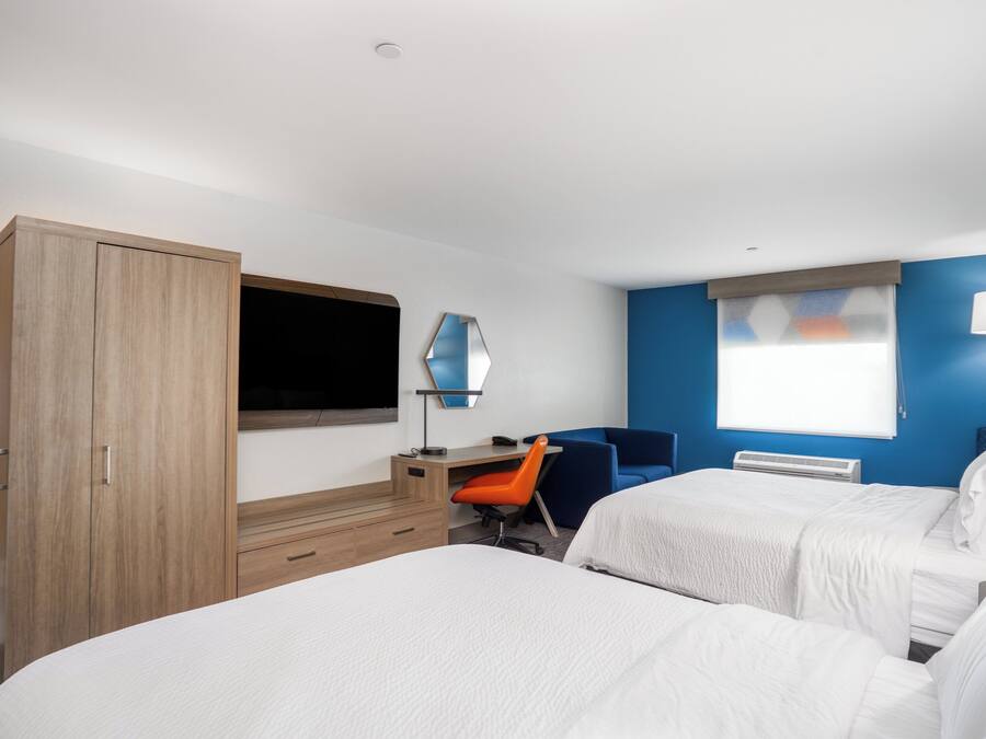 A hotel room with two beds, a desk with a chair, a TV, and a window with blinds.