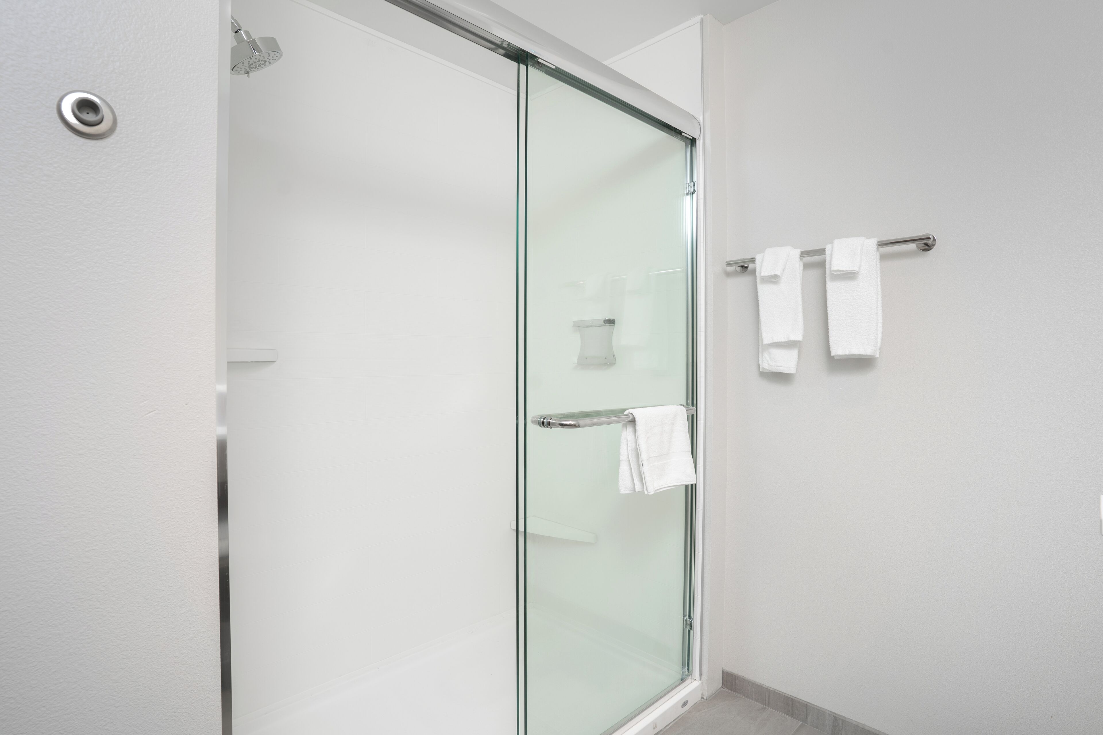 Un baño moderno con cabina de ducha de vidrio, un perchero con dos toallas y una pared blanca.