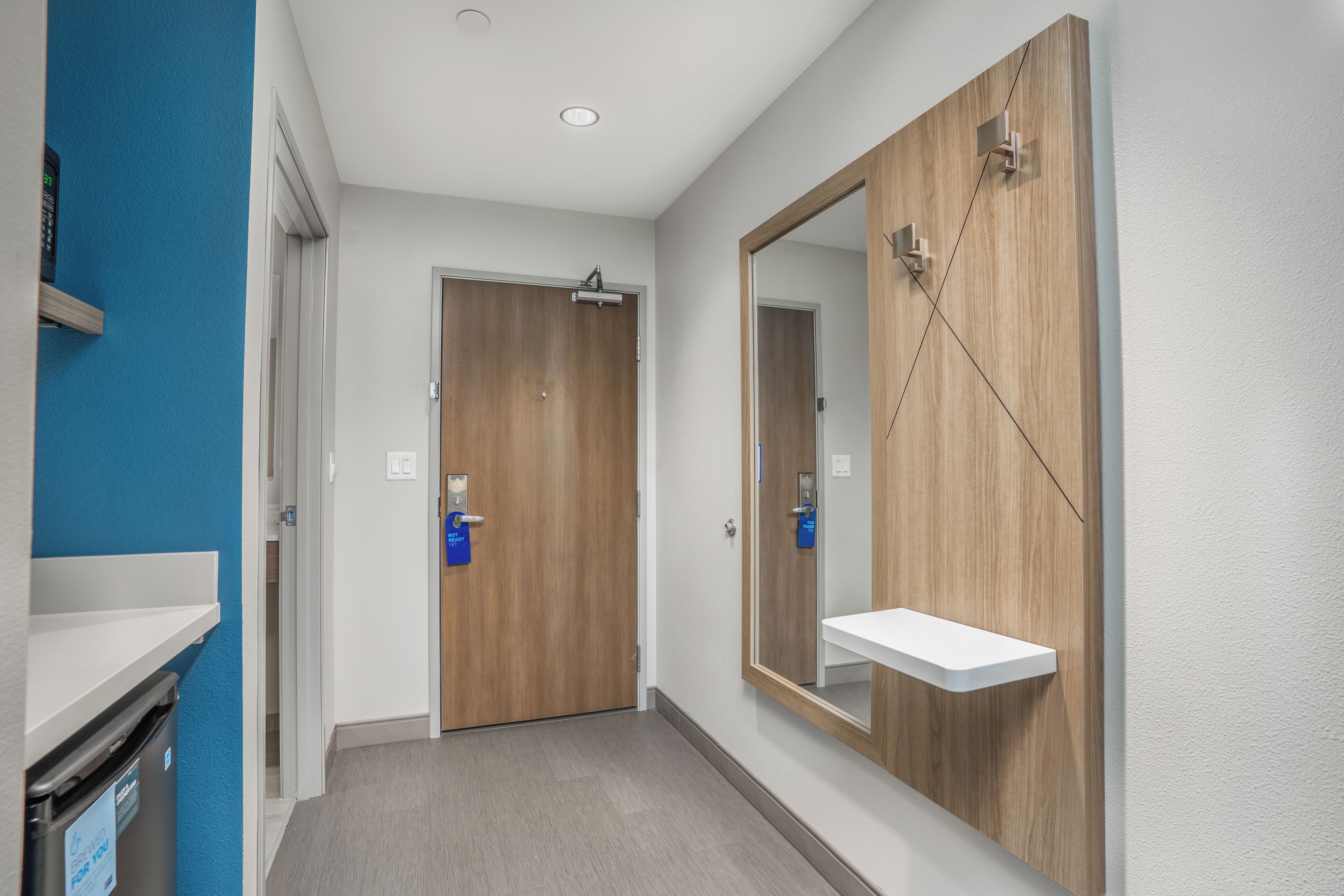 A hallway with a wooden door, a white sink with a mirror, and a blue wall.