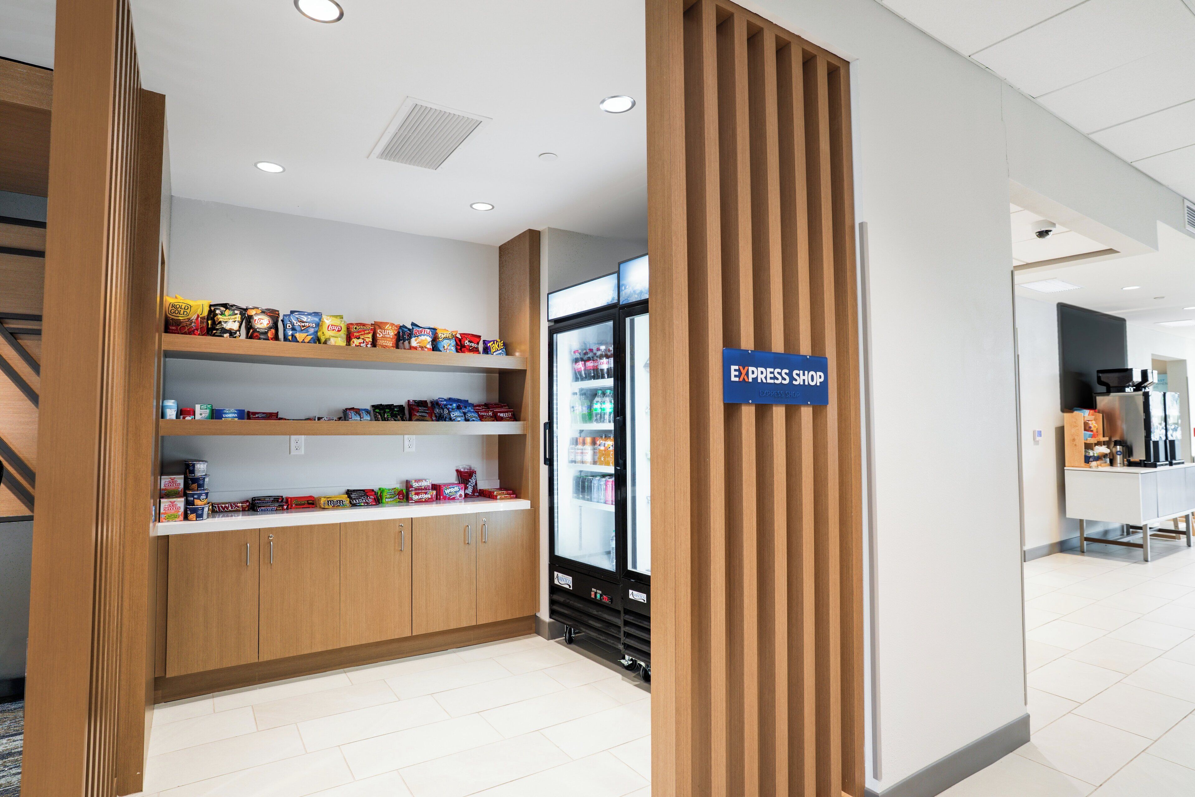 A clean, modern retail area with wooden shelving stocked with snacks and a refrigerated display.