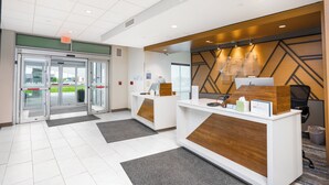 A reception area with a glass door entrance, a reception desk, and a wall-mounted computer station. - Holiday Inn Express & Suites Cedar Rapids NE – Marion by IHG (Marion)