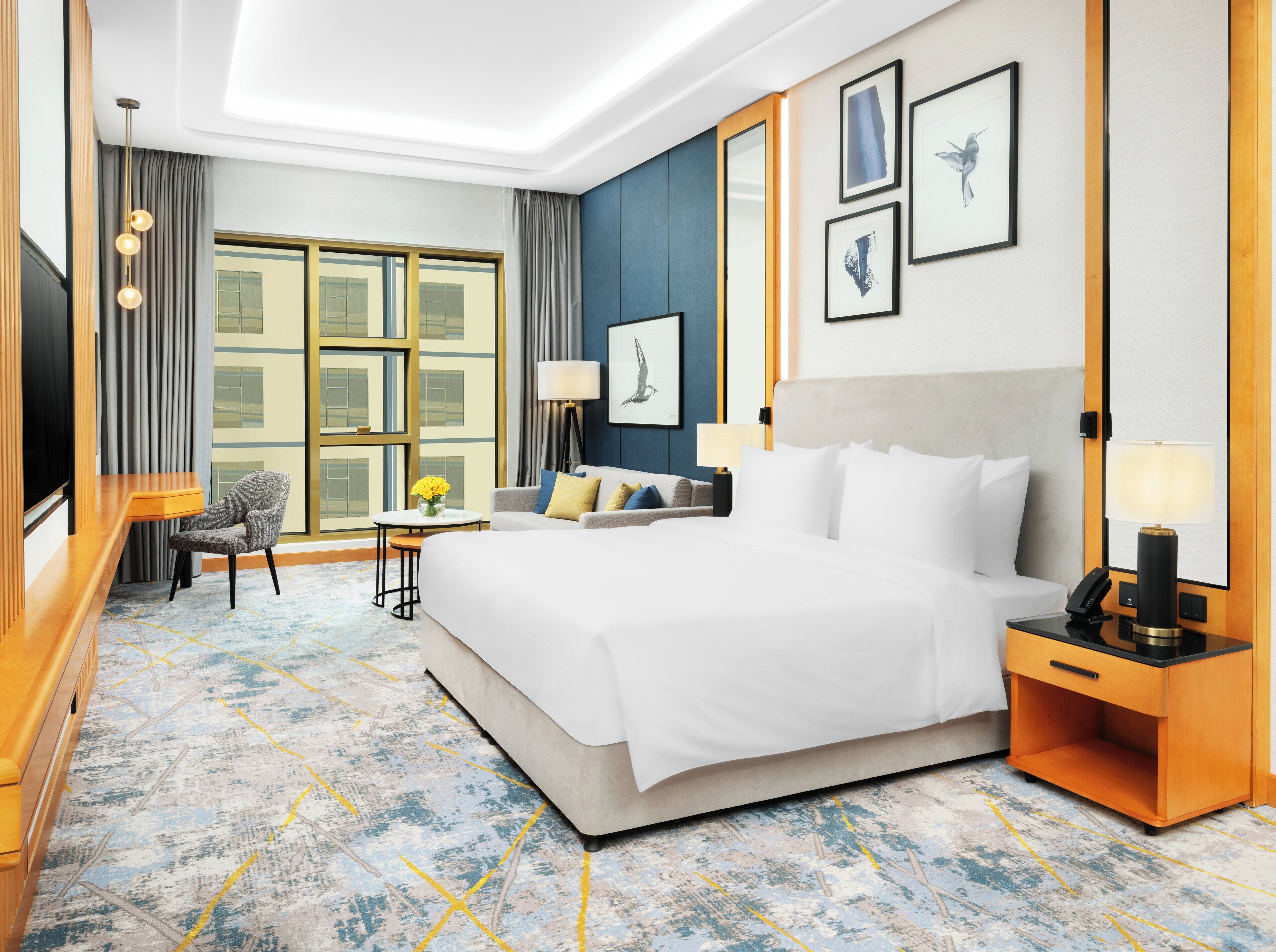 A hotel room with a large bed, a desk, a chair, a TV, and a window with curtains.
