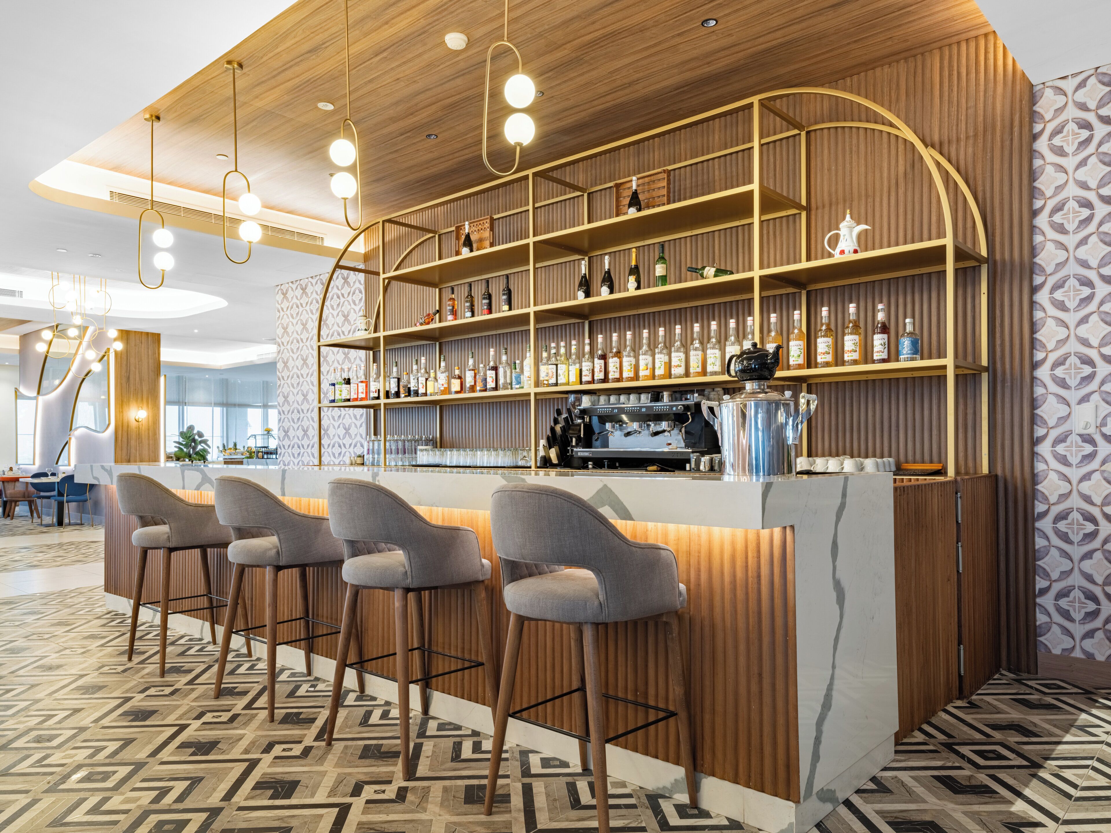 Un espace bar doté d’un comptoir en bois, de plusieurs étagères remplies de bouteilles et de tabourets de bar.