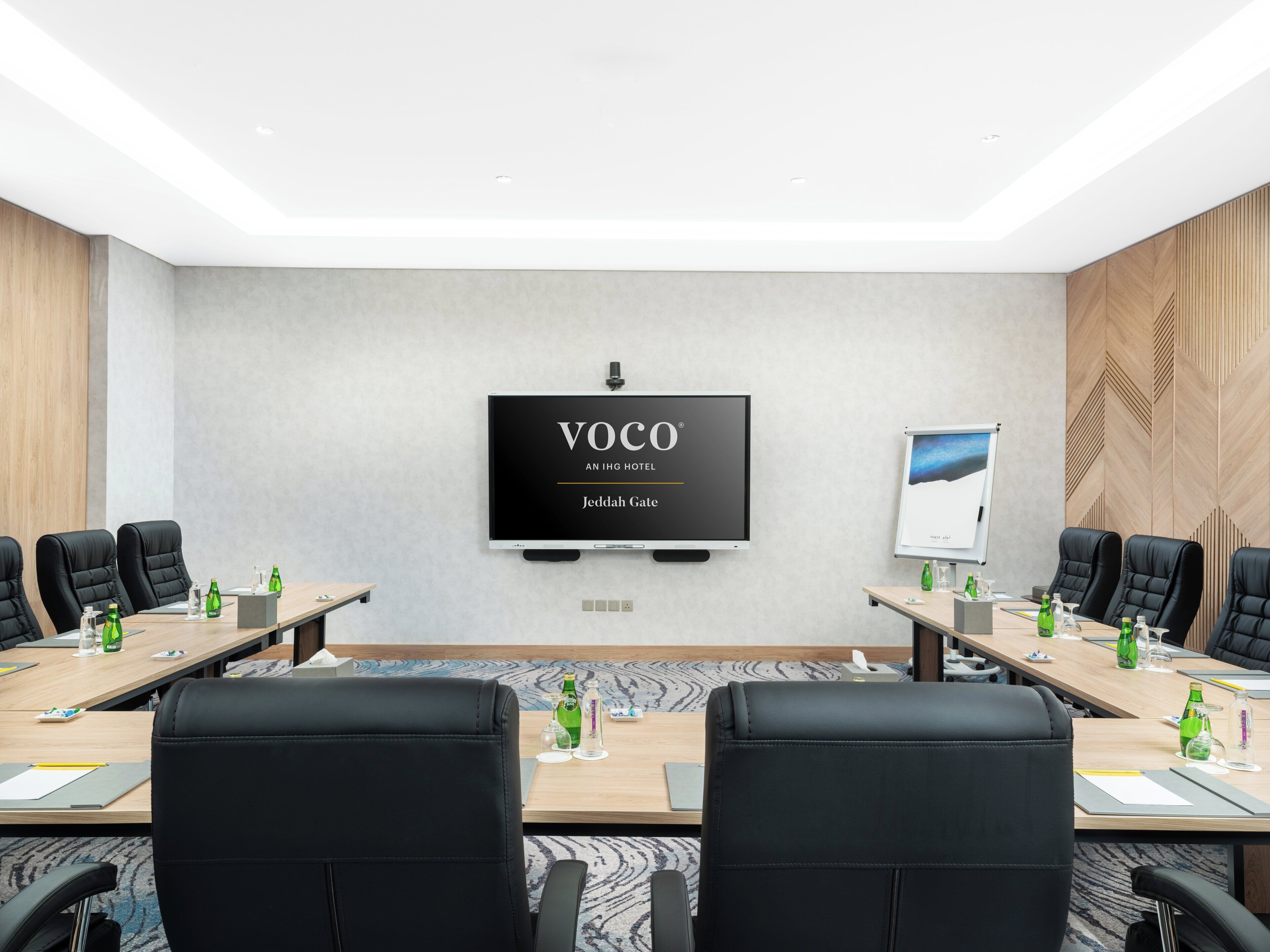 A conference room with a large flat-screen TV displaying "VOCO AN IHG HOTEL Jeddah Gate".