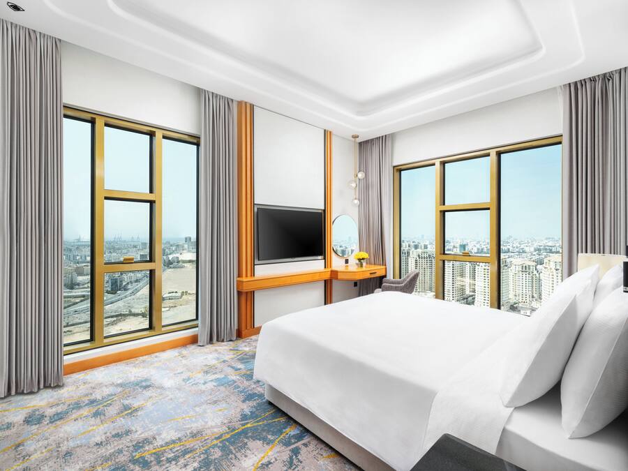 A hotel room with a large bed, a TV, a desk, and a city view.