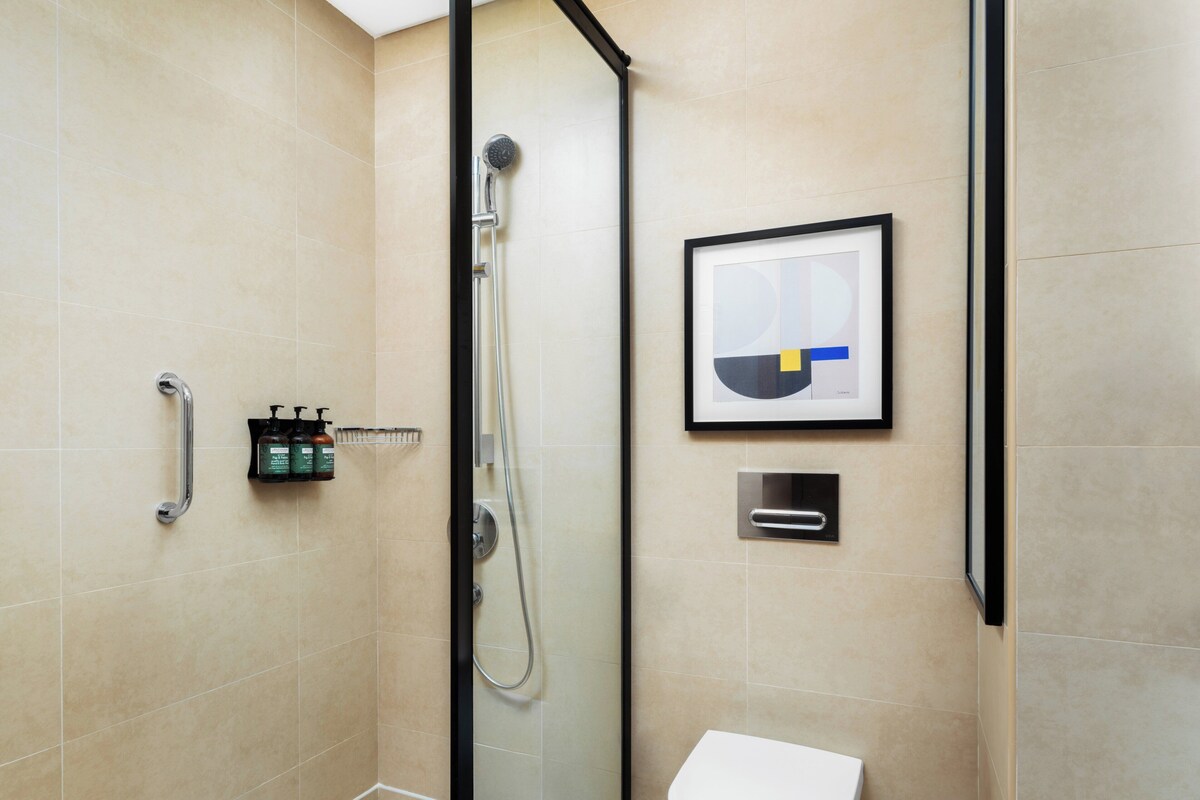 A modern bathroom with a glass-enclosed shower, a white toilet, and a framed abstract artwork on the wall.