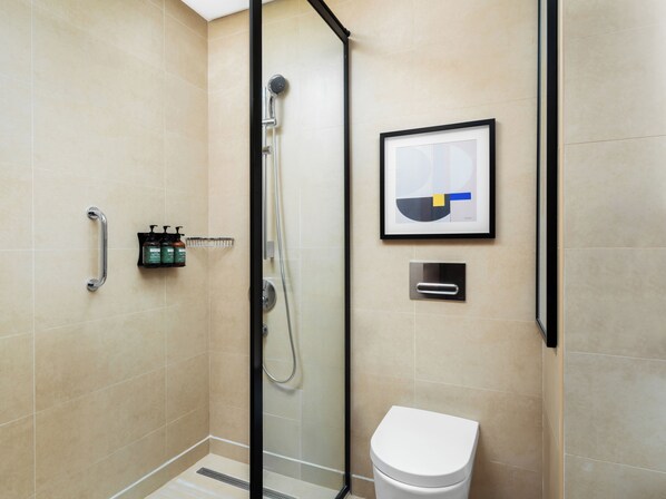 A modern bathroom with a glass-enclosed shower, a white toilet, and a framed abstract artwork on the wall. - voco Jeddah Gate by IHG (Jeddah)