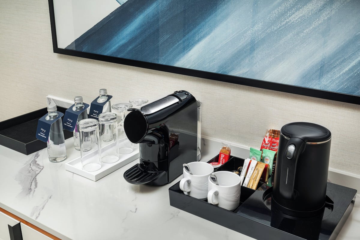 A hotel room's coffee station with a coffee maker, cups, and coffee pods.