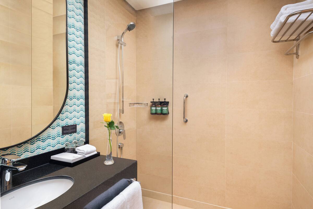 A modern bathroom with a large mirror, a sink, a shower, and a towel rack.