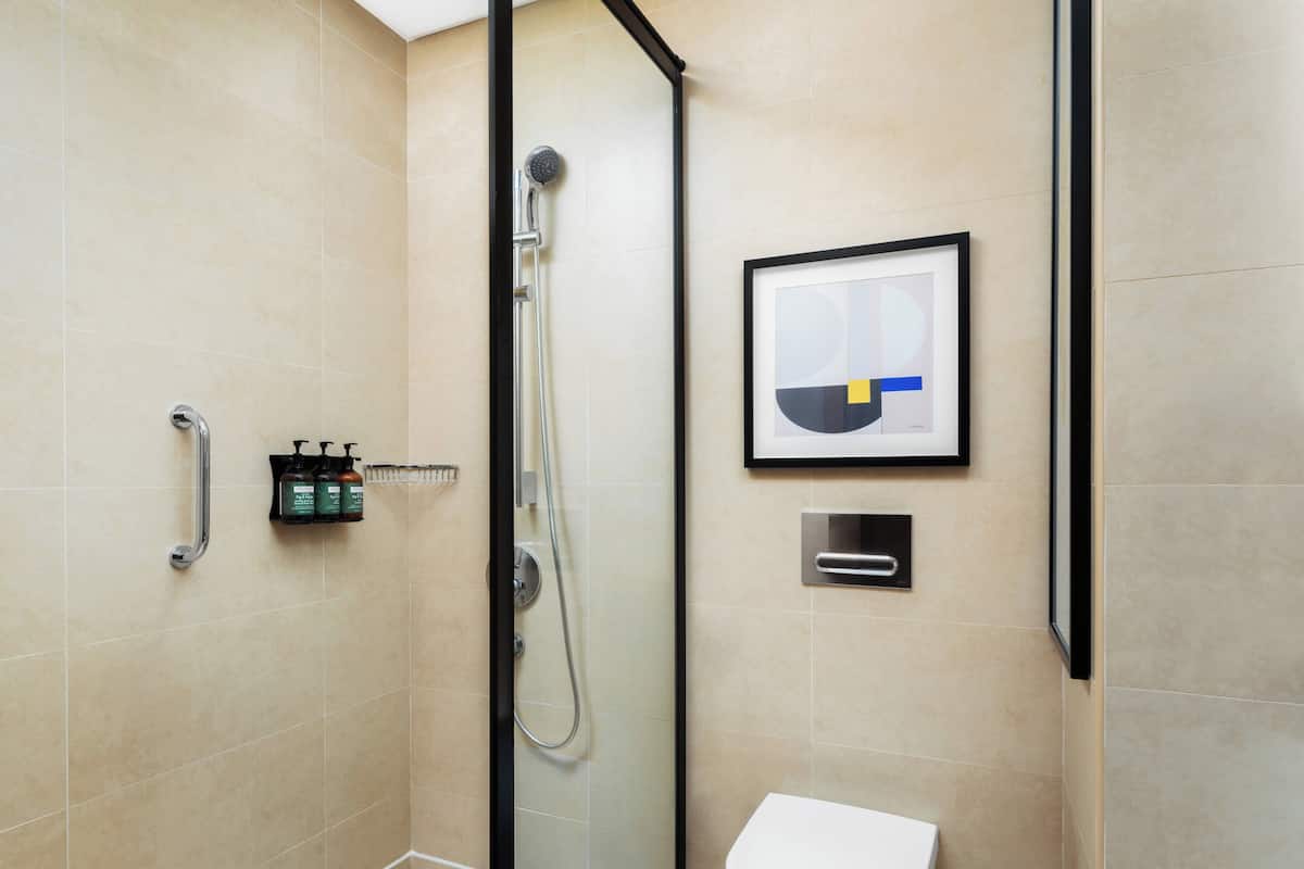 A modern bathroom with a glass-enclosed shower, a white toilet, and a framed abstract artwork on the wall.
