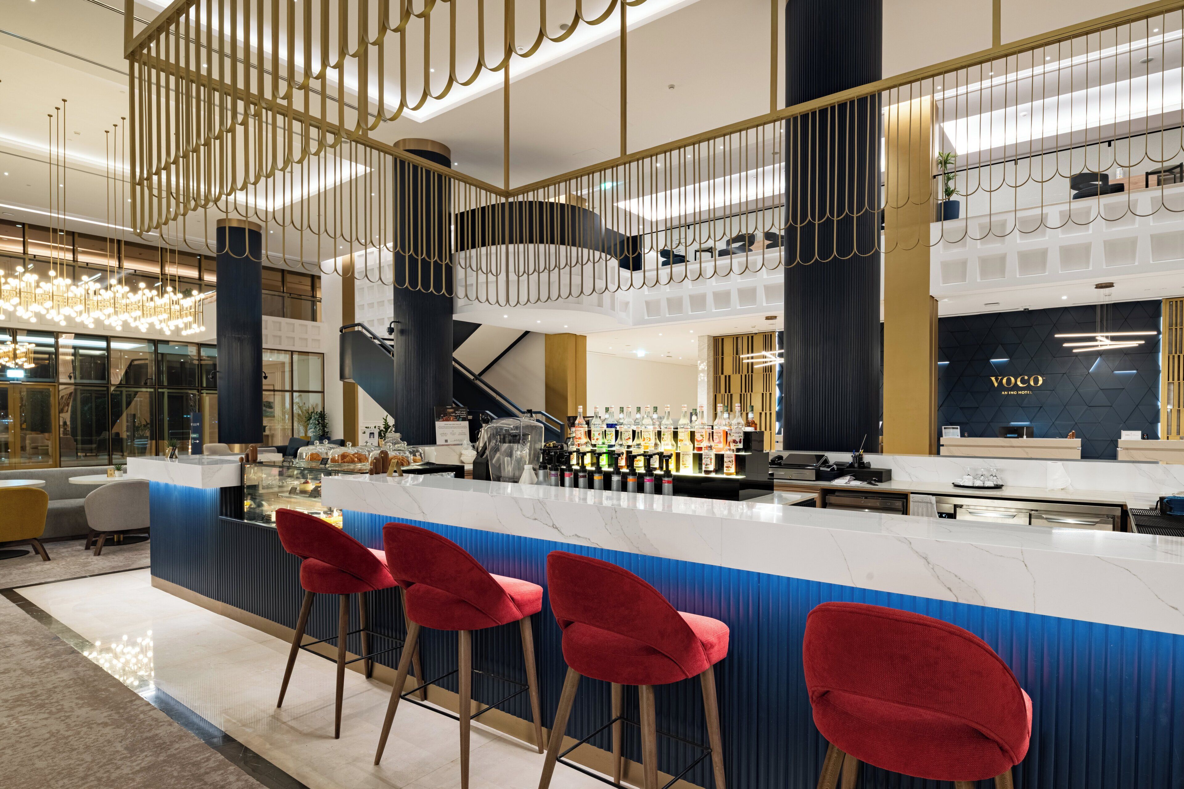 Uma área de bar moderna com bancada de mármore, banquetes vermelhos e uma escada com guarda-corpo.