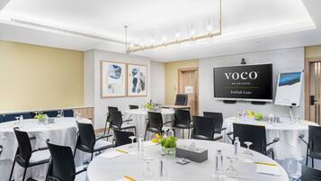A conference room with round tables, black chairs, and a large screen displaying the hotel name.