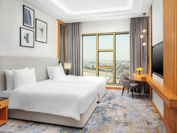 Une chambre d’hôtel avec un grand lit, un bureau avec une chaise, une télévision et une vue sur la ville grâce à de grandes fenêtres.