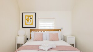 A neatly made bed with pink and white bedding, a framed picture on the wall, and a window with blinds. - The Sakura Mews by Harrods (London)