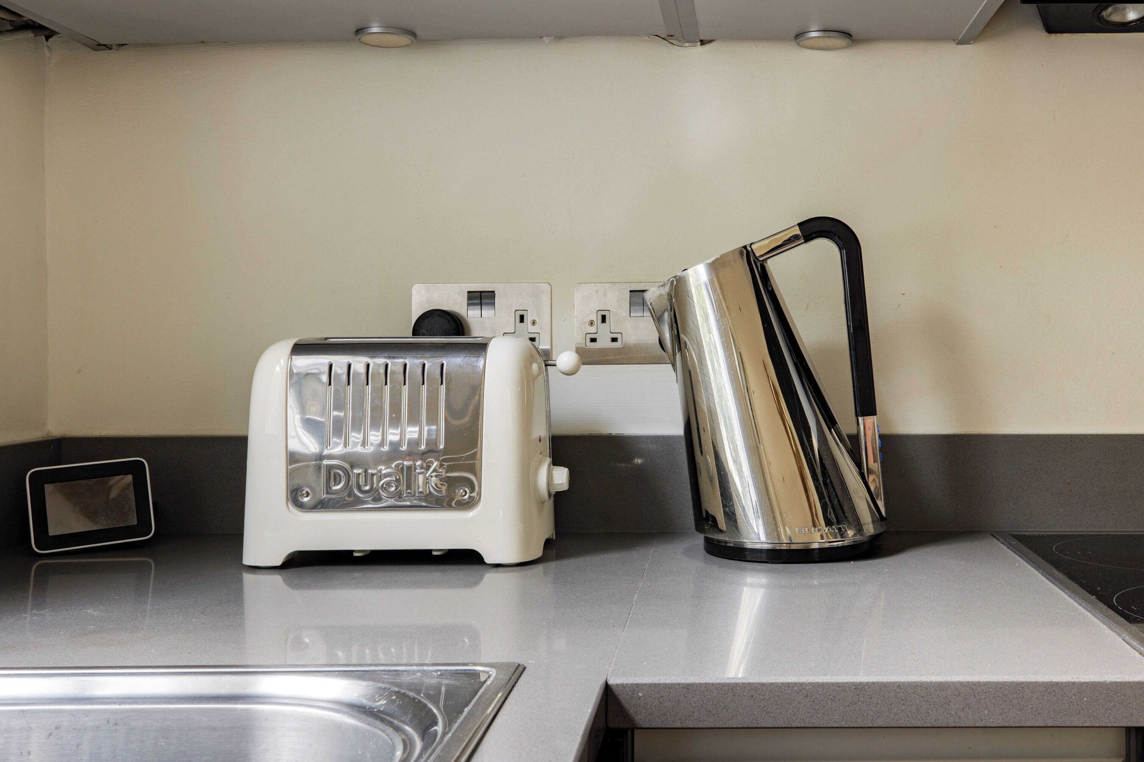 A kitchen with a white toaster, a stainless steel kettle, and a power outlet on the counter.