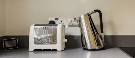 A kitchen with a white toaster, a stainless steel kettle, and a power outlet on the counter.