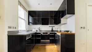 A modern kitchen with black cabinetry, a wooden countertop, and a built-in oven. - The Sakura Mews by Harrods (London)