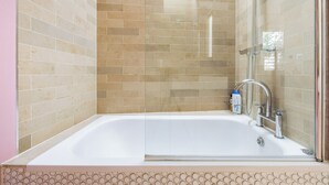 A modern bathroom with a glass-enclosed shower, a white bathtub, and beige tiled walls. - The Sakura Mews by Harrods (London)
