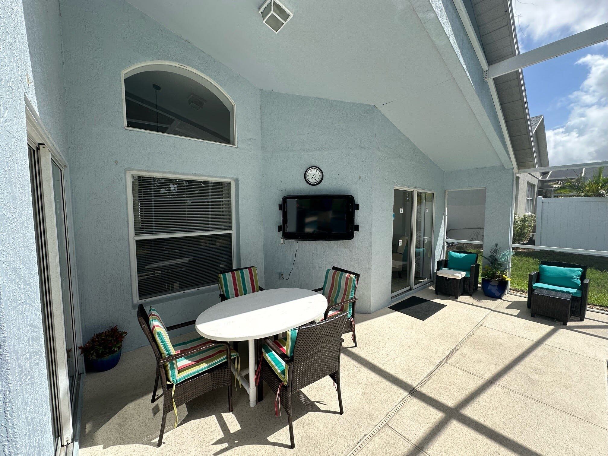 Un patio couvert avec une table et des chaises, un téléviseur fixé au mur et une porte-fenêtre coulissante.