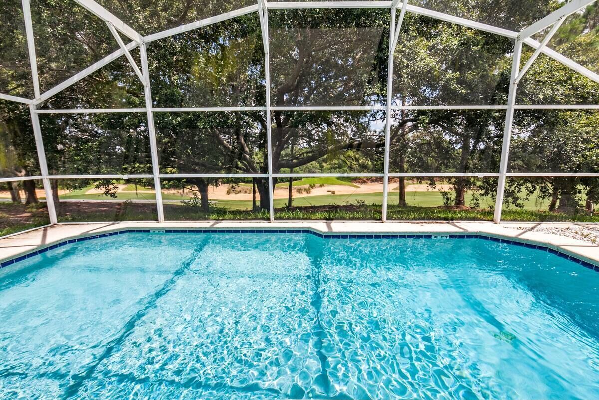 A swimming pool with a clear view of a golf course through a white fence.