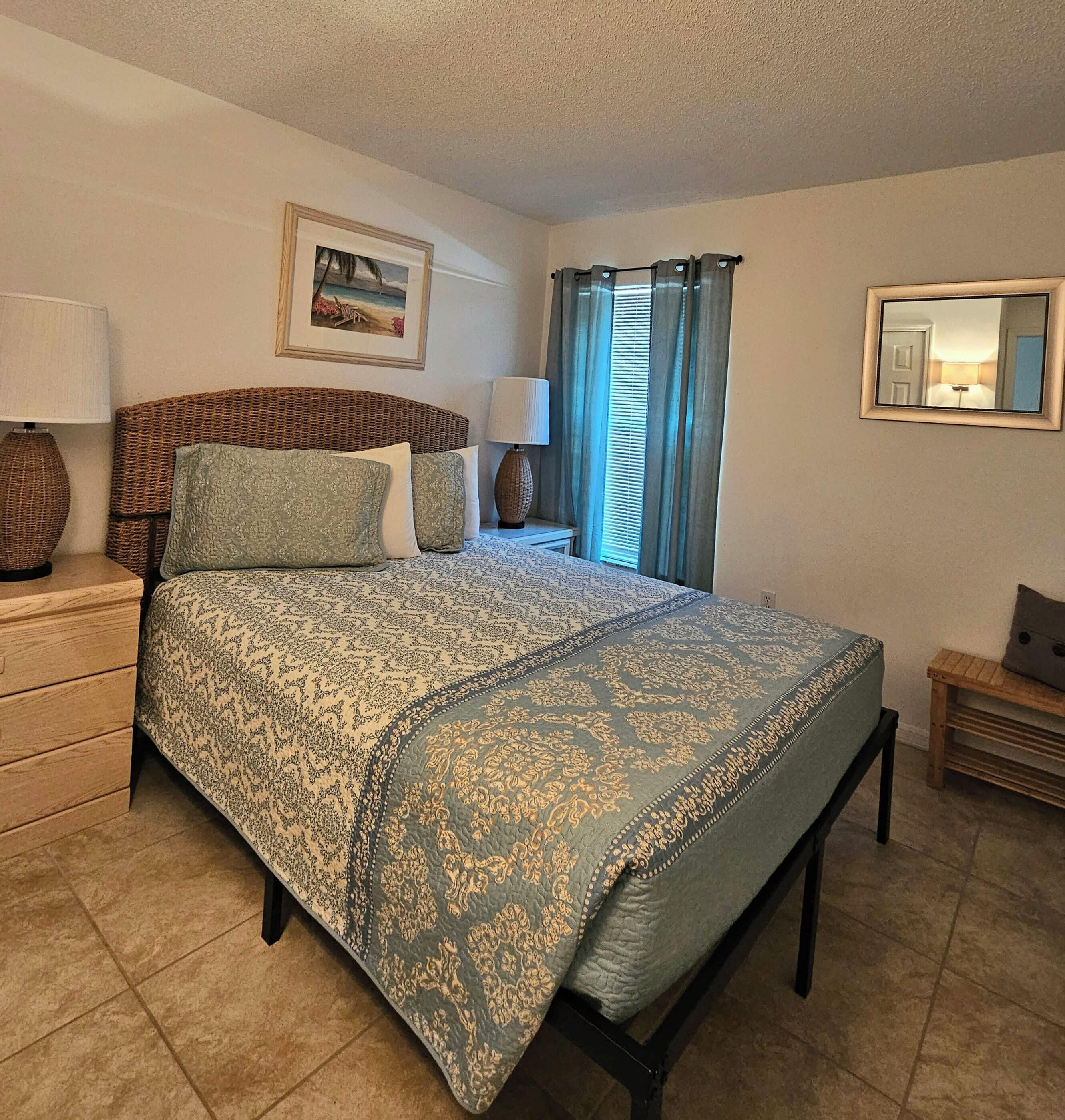 A neatly arranged bedroom with a bed, bedside tables, a lamp, a framed picture on the wall, and a mirror.