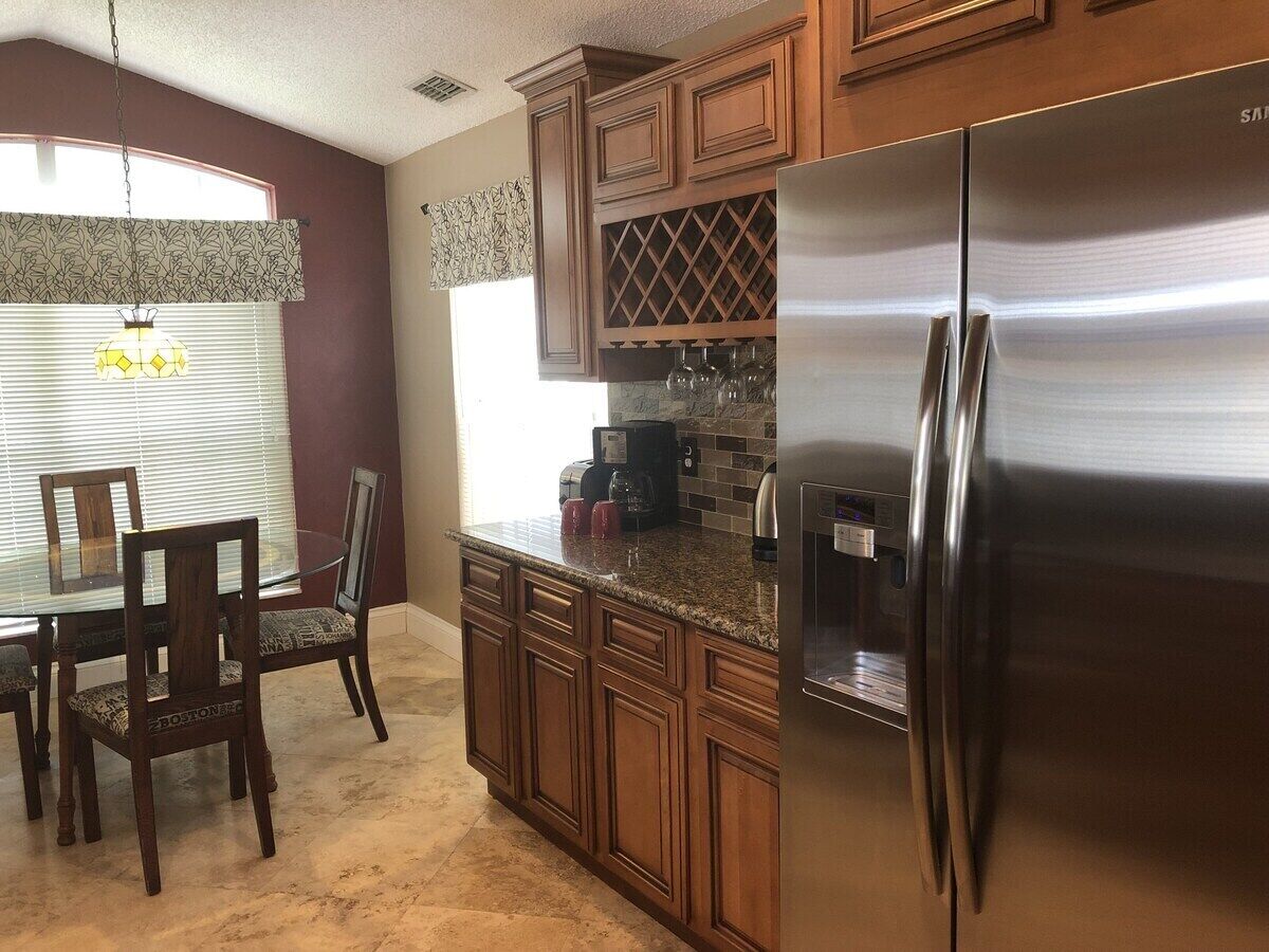 A kitchen with wooden cabinets, a stainless steel refrigerator, a dining table with chairs, and a wine rack above the counter.