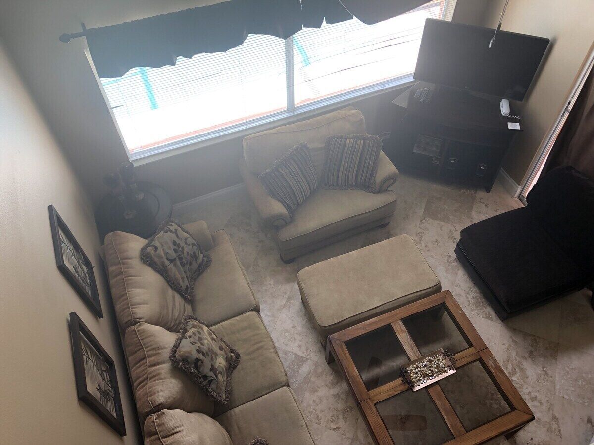 A living room with a sofa, ottoman, and a coffee table. There are framed pictures on the wall and a television on a stand.