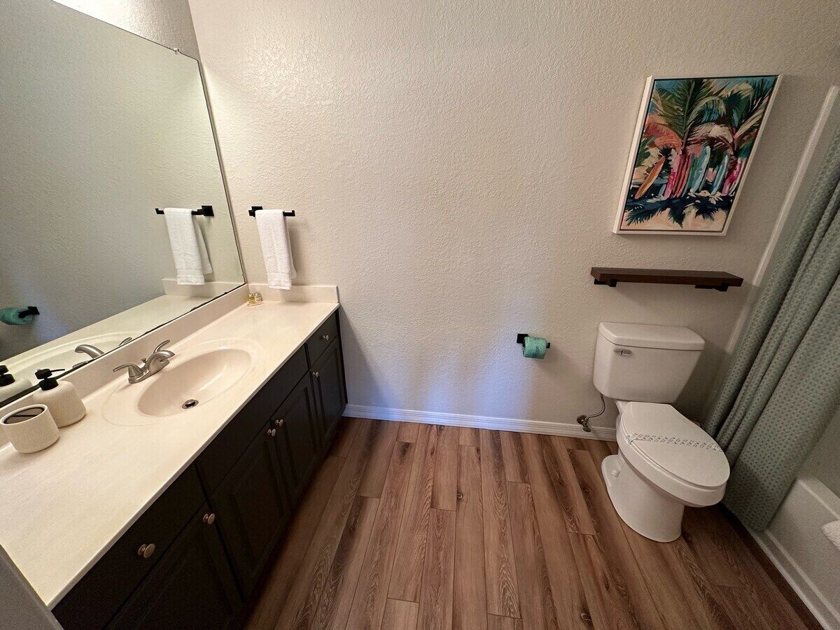Une salle de bain avec un plancher en bois, un lavabo blanc, des toilettes et un miroir.
